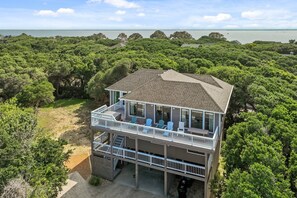 A two-story beachfront house with a balcony, surrounded by dense greenery and a view of the ocean. - 2444 - Sea Forever, - Large Oceanside Getaway Steps to the Beach (Duck)