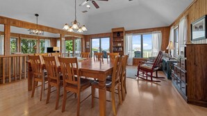 Un comedor espacioso con muebles de madera, ventilador de techo y ventanas amplias que dan a vistas del exterior.