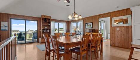 A spacious dining area with a large wooden table and chairs, a ceiling fan, and a view of the outdoors.