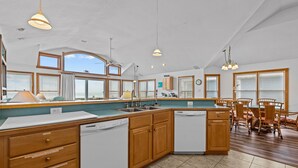 A spacious kitchen with wooden cabinets, a large island, and a dining area with chairs. - 5785- Southern Comfort - South Nags Head Oceanfront Retreat (Nags Head)