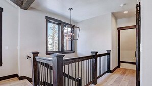 A staircase with a wooden railing, a window with a view of trees, and a ceiling light fixture.