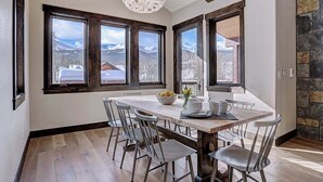 A dining area with a large table, multiple chairs, and a view of mountains through large windows.
