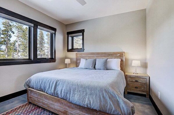 A bedroom with a large bed, two bedside lamps, a nightstand, a window, and a view of trees.