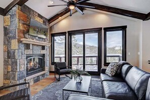 Una sala de estar acogedora con chimenea de piedra, sofá de cuero y ventanas amplias que dan a un paisaje exterior.
