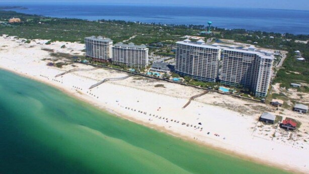 Vista aérea de una zona costera con dos grandes edificios de hotel, una playa de arena y una vista despejada del océano.