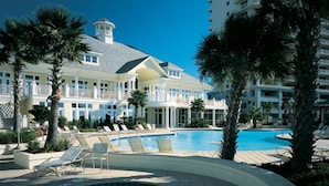 Un resort con una piscina grande, palmeras y un edificio de varios pisos con balcones.