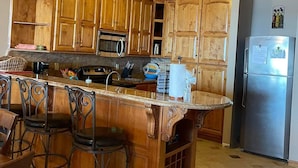 A kitchen with wooden cabinets, a stainless steel refrigerator, and a bar area with stools.