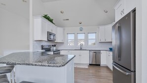 Uma cozinha moderna com armários brancos, bancadas de granito e eletrodomésticos de aço inoxidável, e uma ilha central com banquetas.