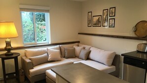 En moderne stue med en beige hjørnesofa, et lille rundt bord med en lampe, et spisebord og en opvaskemaskine.