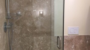 Et badeværelse med en glasafskærmet brusekabine, et toilet og en vægmonteret lysarmatur.