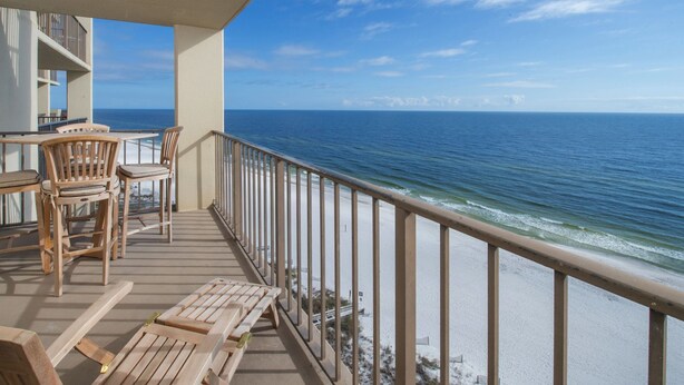 A balcony with wooden furniture, a view of the ocean, and a clear sky.