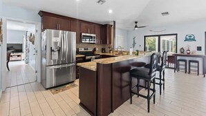 A modern kitchen with dark wooden cabinets, stainless steel appliances, and a central island with bar stools. - Sombrero Beach | Canalfront Pool Home + Dock (Marathon)