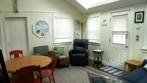 A cozy living room with a wooden dining table, red chairs, a blue sofa, and a black leather armchair. - Peaceful 2 Bdrm Cottage WiFi A/C Ingrd Pool & Walk To Beach! (Dennis)