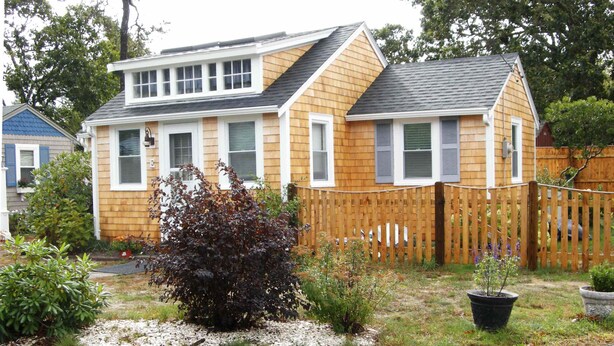 A two-story house with a wooden exterior, a fenced backyard, and a variety of plants. - Peaceful 2 Bdrm Cottage WiFi A/C Ingrd Pool & Walk To Beach! (Dennis)