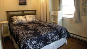 A bedroom with a bed, a nightstand, a window with curtains, and a wall-mounted shelf. - Peaceful 2 Bdrm Cottage WiFi A/C Ingrd Pool & Walk To Beach! (Dennis)