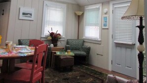 A room with a skylight, a dining area with a table and chairs, a patterned rug, and a green armchair. - Peaceful 2 Bdrm Cottage WiFi A/C Ingrd Pool & Walk To Beach! (Dennis)