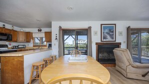 Uma cozinha com armários de madeira, uma mesa de jantar com cadeiras, uma lareira e vista através das portas de vidro.