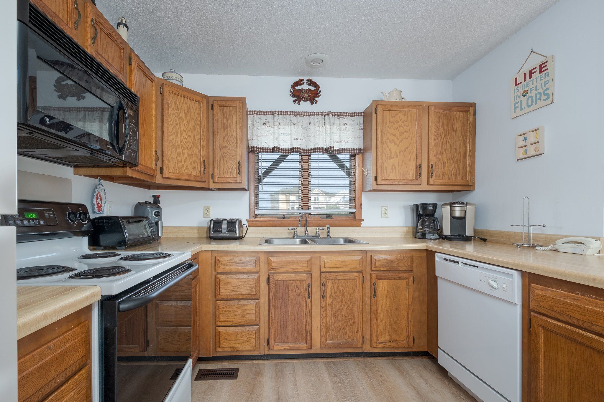A compact kitchen with wooden cabinets, a microwave, a toaster, a sink, and a dishwasher.