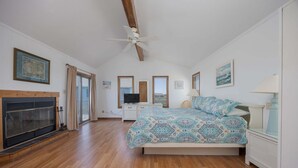 Um quarto com cama, televisão, lareira e ventoinha no teto.