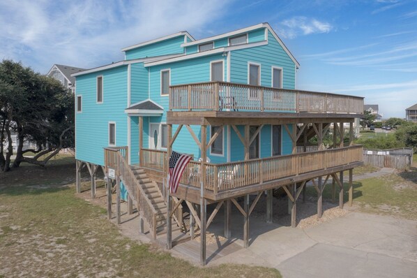 A two-story house with a wooden deck and a staircase leading to the upper level. - 1484 - Beachin' It, Oceanside OBX Beach House w/Private Pool. Family Fun! (Corolla)