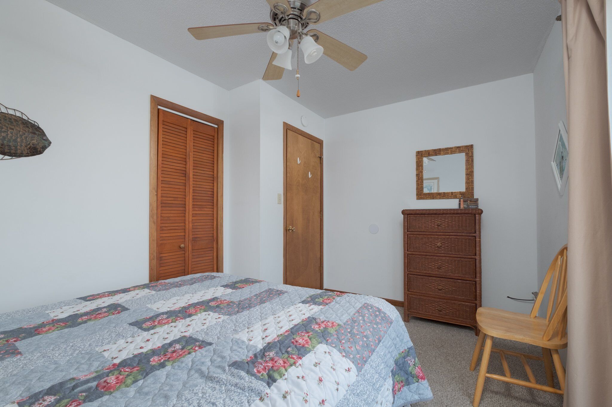 A bedroom with a bed, a dresser, a chair, and a ceiling fan.