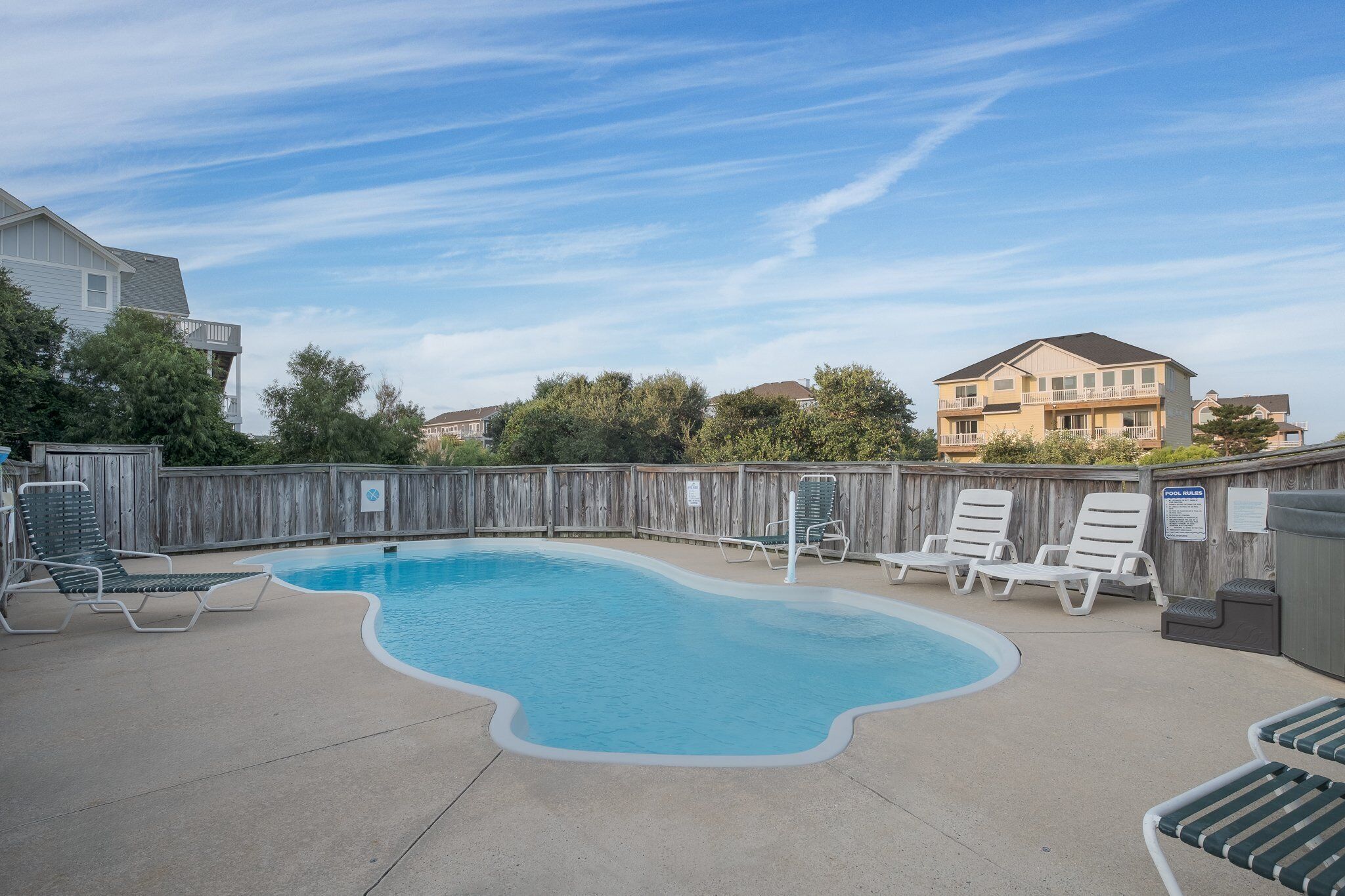 A swimming pool with lounge chairs, a wooden fence, and a sign indicating a pool area.