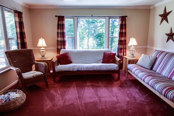 A cozy room with a red carpet, a white sofa, a striped sofa, a wicker chair, and two lamps.
