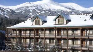 Eine mehrstöckige Lodge mit verschneitem Dach, hölzernen Balkonen und einem Berg im Hintergrund, der mit Schnee bedeckt ist.