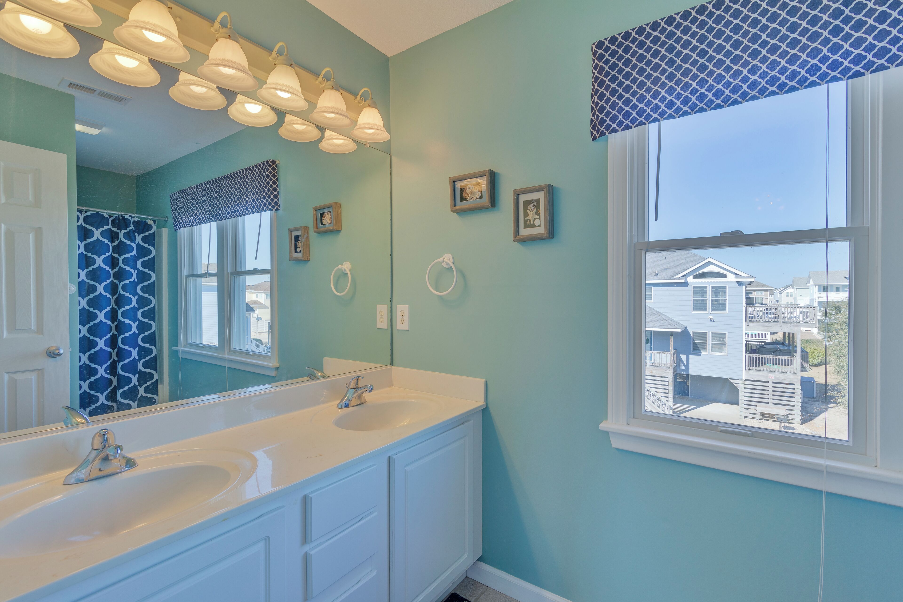 A bathroom with two sinks, a large mirror, and a window with a view of houses.