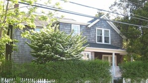 A two-story house with a white picket fence, a front porch, and a large evergreen tree.
