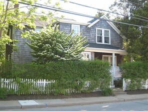 Charming home with a front porch, white picket fence, and a large evergreen tree.