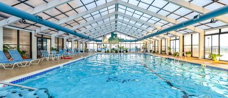 An indoor swimming pool with clear lanes, lounge chairs, and potted plants.
