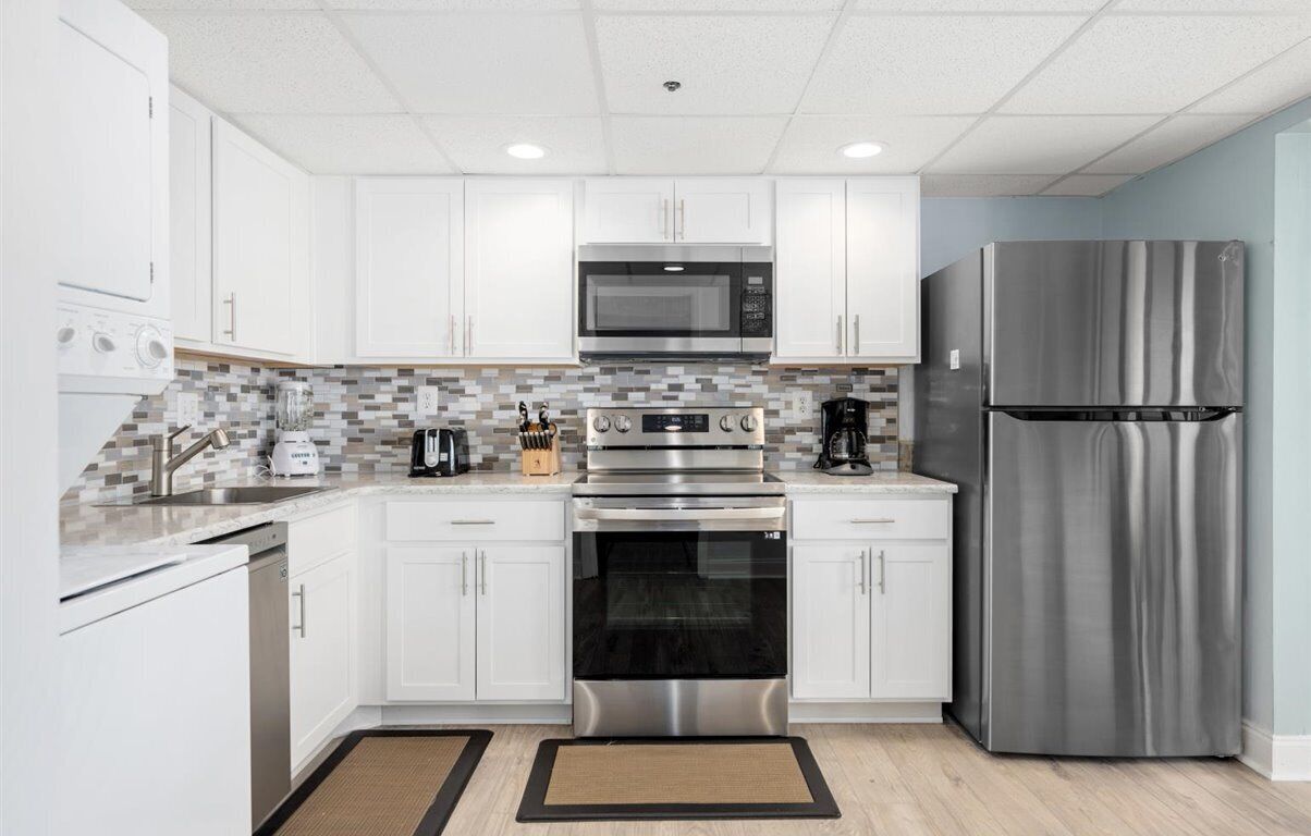 A modern kitchen with white cabinets, stainless steel appliances, and a tiled backsplash.