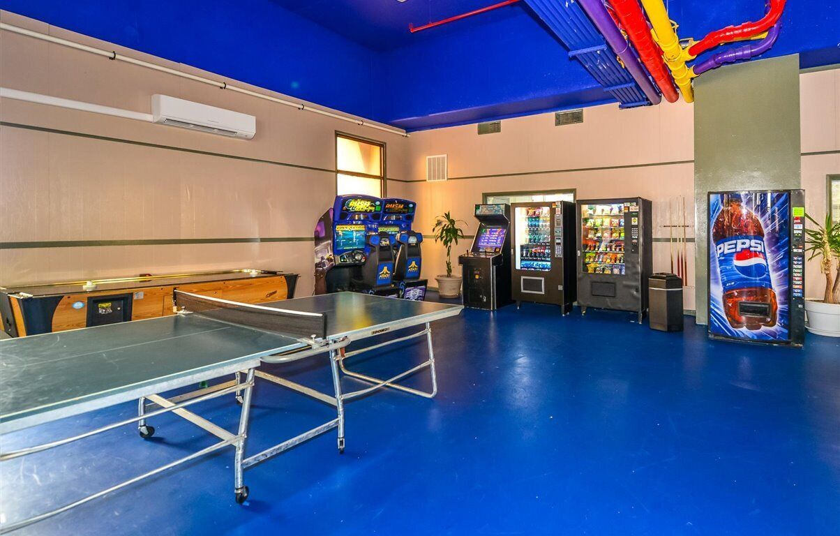 A room with a ping pong table, arcade games, vending machines, and a Pepsi refrigerator.