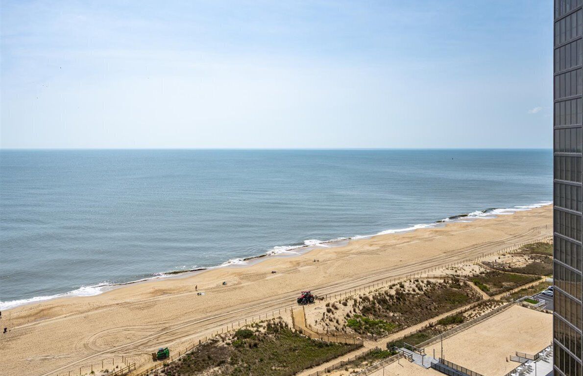 A beach view with a sandy shore, a clear sky, and a building in the foreground.