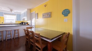 A kitchen with a yellow wall, wooden chairs, a glass-top table, and a ceiling fan. - 5232- Peaceful Easy Feeling - Kill Devil Hills Home | Dog-Friendly & Beach Walk (Kill Devil Hills)