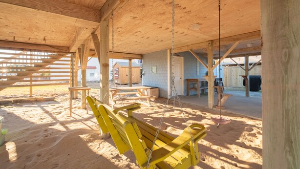 A spacious indoor area with wooden beams, a swing, and a sandbox. - 5232- Peaceful Easy Feeling - Kill Devil Hills Home | Dog-Friendly & Beach Walk (Kill Devil Hills)