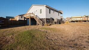 A single-story house with a wooden deck and a staircase leading to a covered porch. - 5232- Peaceful Easy Feeling - Kill Devil Hills Home | Dog-Friendly & Beach Walk (Kill Devil Hills)