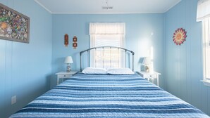 A bedroom with a bed, two bedside tables, a ceiling fan, a window with blinds, and wall decorations. - 5232- Peaceful Easy Feeling - Kill Devil Hills Home | Dog-Friendly & Beach Walk (Kill Devil Hills)