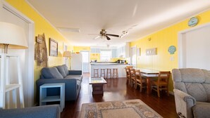 A living room with a sofa, chairs, a coffee table, and a rug. There is a kitchen area with a dining table and chairs in the background. - 5232- Peaceful Easy Feeling - Kill Devil Hills Home | Dog-Friendly & Beach Walk (Kill Devil Hills)