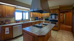 A modern kitchen with wooden cabinets, a stainless steel range hood, a dishwasher, and a large island with a tiled countertop.
