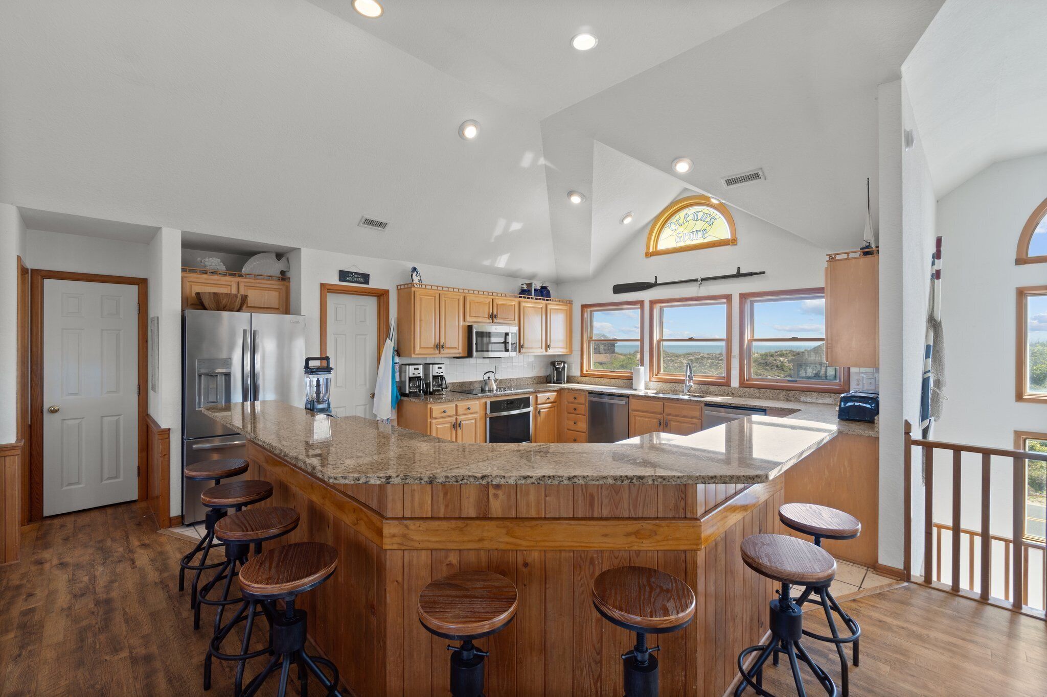A spacious kitchen with a large island, wooden bar stools, and a view of the outdoors.