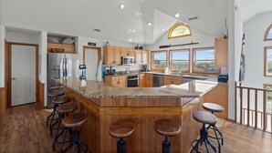 A spacious kitchen with a large island, wooden bar stools, and a view of the outdoors.