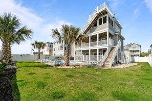 A multi-story beachfront property with a pool, palm trees, and a white fence. - 5409- Latitude Adjustment - Dog-Friendly Nags Head Home w/ Private Pool (Nags Head)