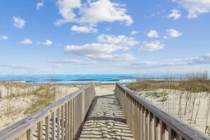 A wooden boardwalk leading to a beach with sand and sparse vegetation.