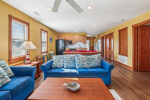 A compact living space with a kitchenette, a blue sofa, a wooden coffee table, and a ceiling fan.