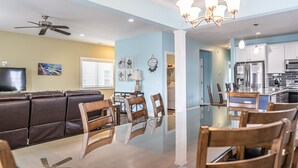 A modern living room with a glass dining table, brown leather sofa, and a ceiling fan.