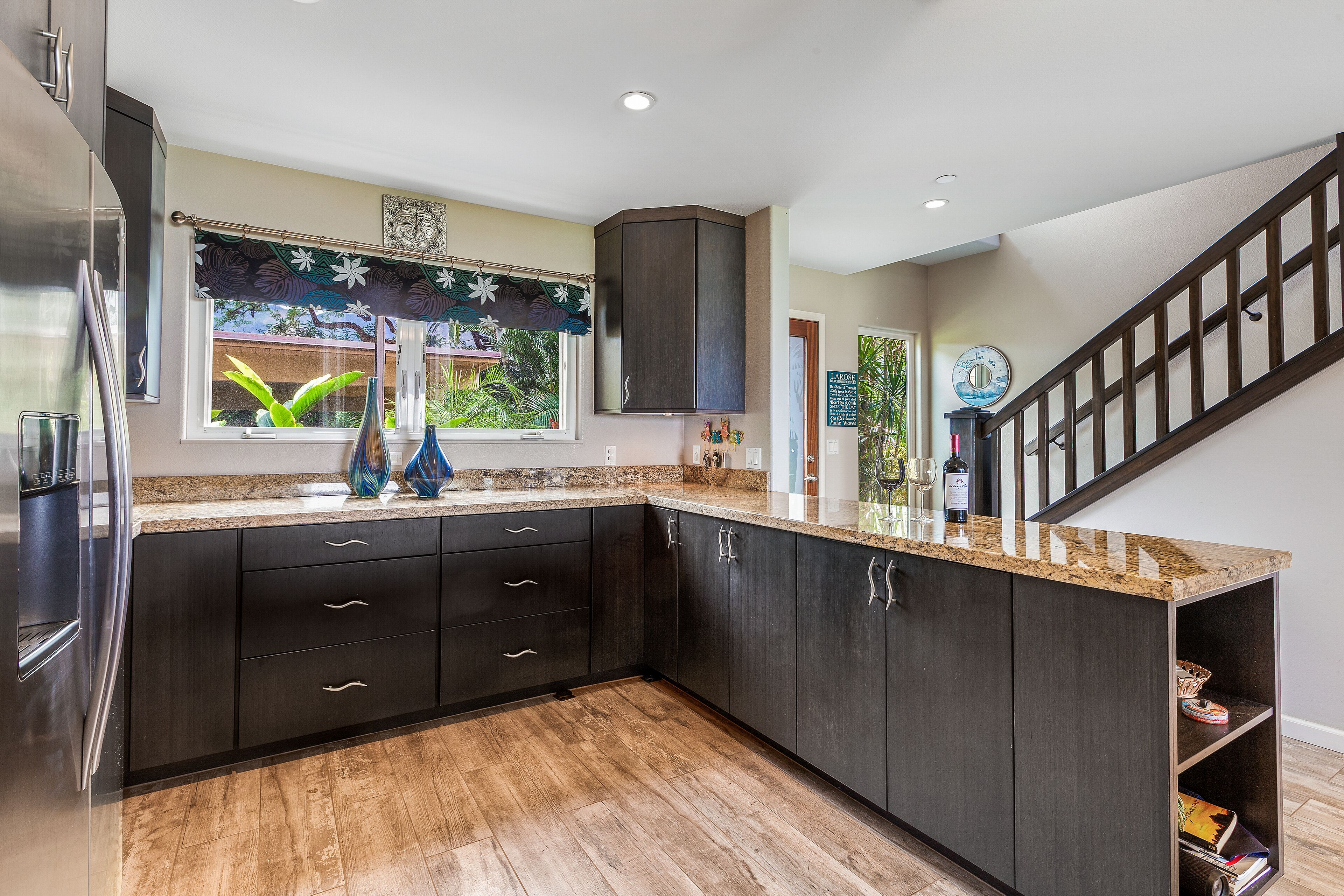 A modern kitchen with dark cabinetry, a granite countertop, and a wooden floor.