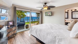 A bedroom with a large bed, a ceiling fan, a view of the ocean, and a balcony with a chair.