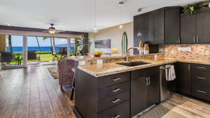 A modern kitchen with dark cabinetry, a granite countertop, and a view of the ocean.